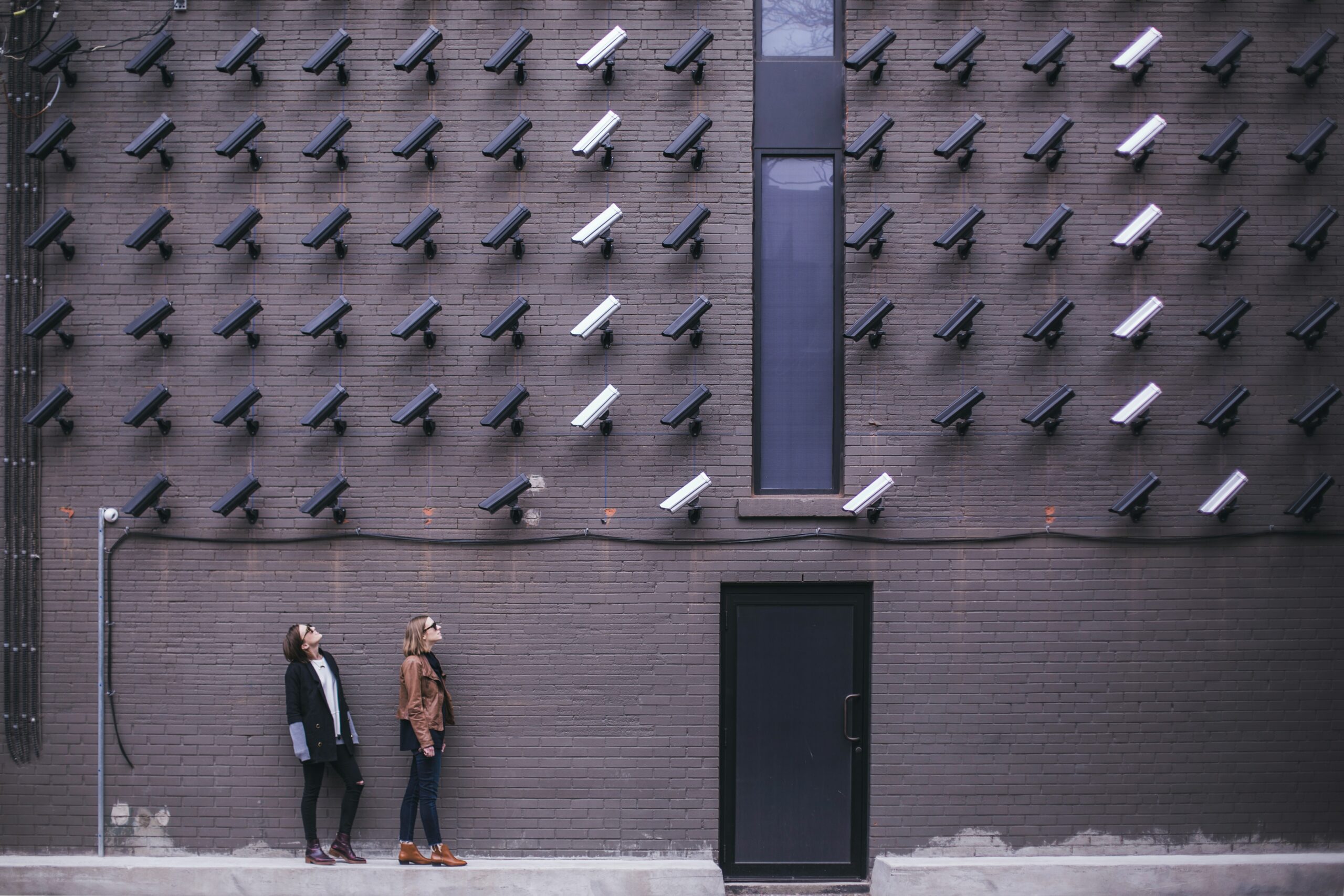 Women looking at surveillance cameras on a gray wall.
